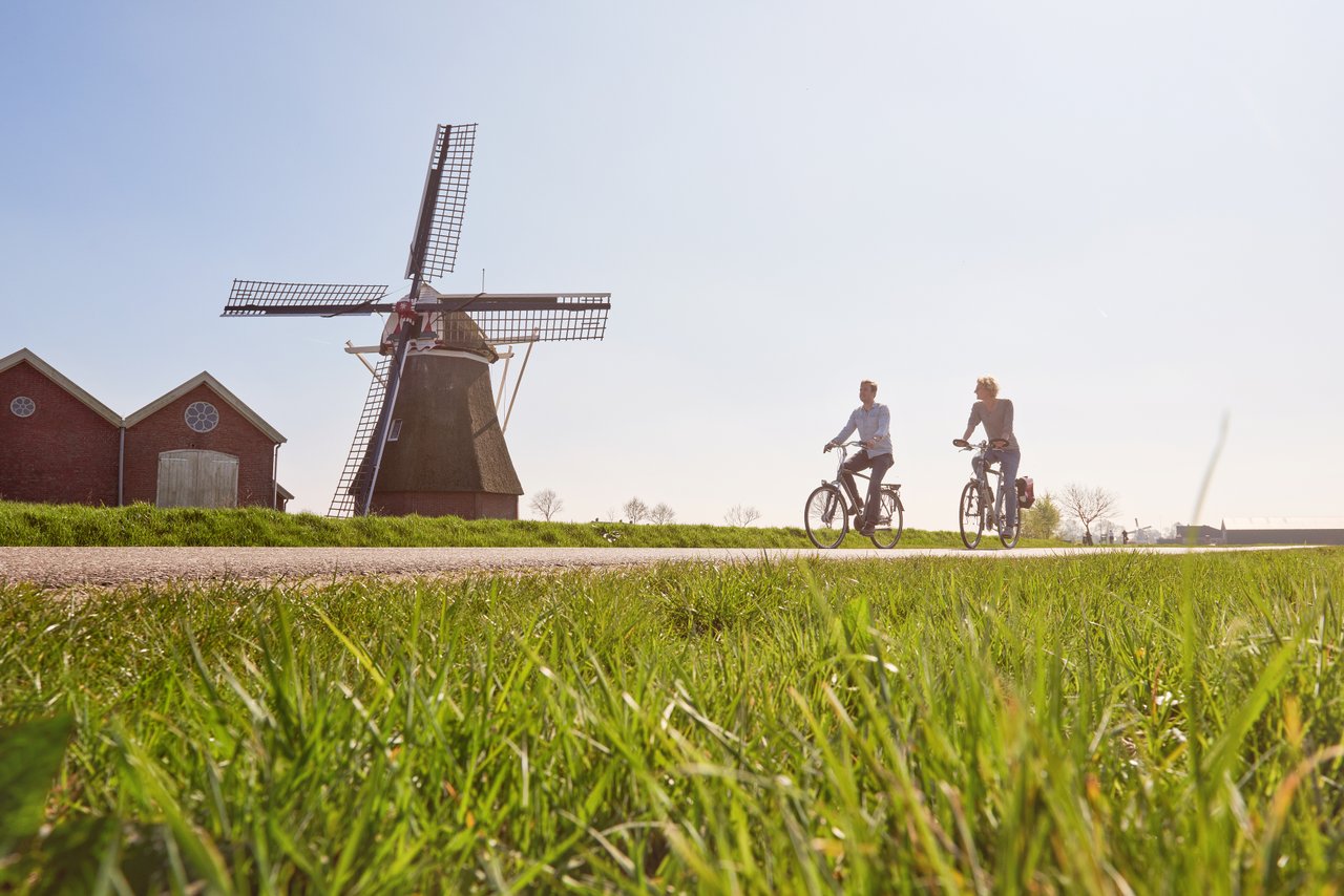 man en vrouw fietsen langs een molen